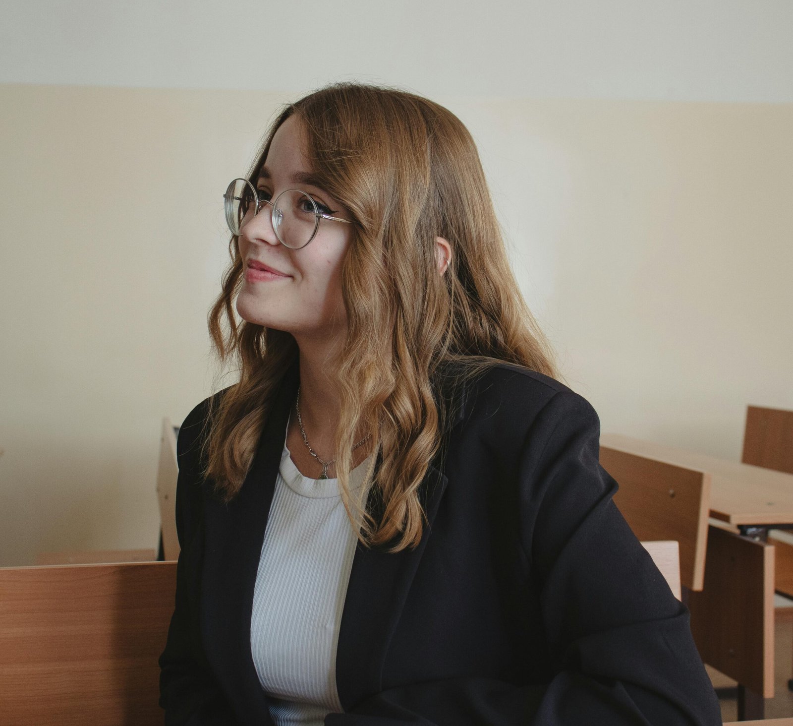 Portrait of a young woman in eyeglasses and black blazer, smiling indoors.